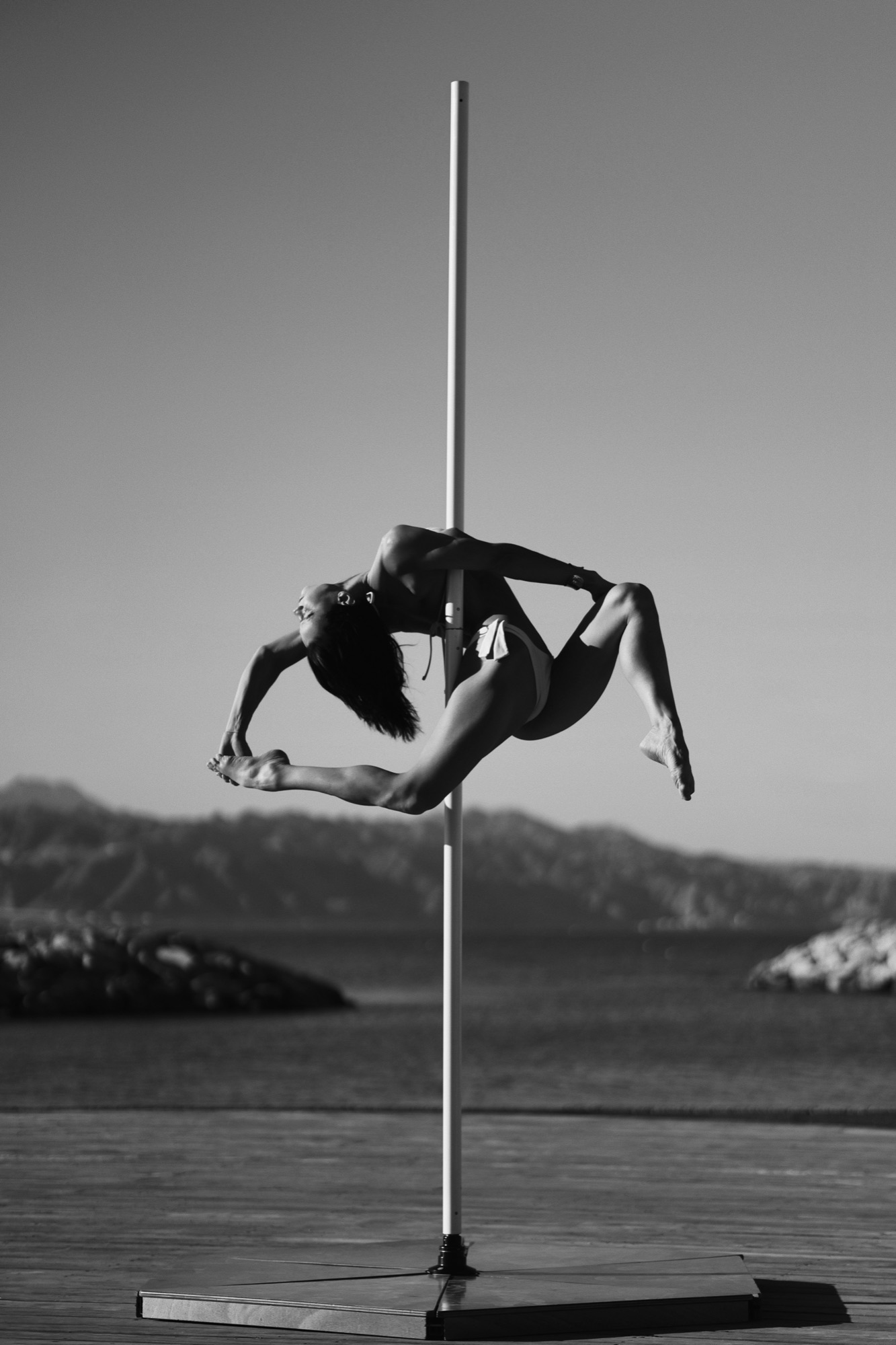 Alisa Pleskova in a backbend on a pole by the sea, black and white