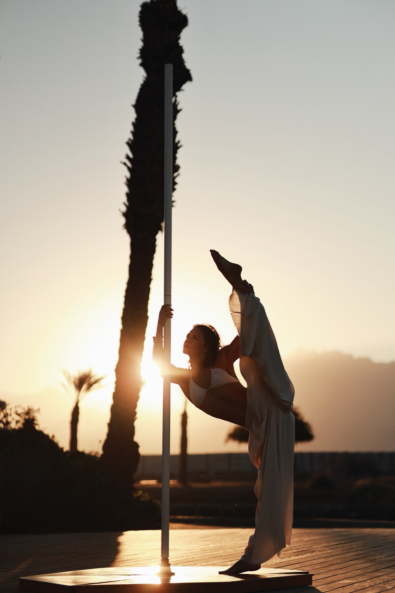Alisa Pleskova holding a standing split at the pole at sunset, in profile